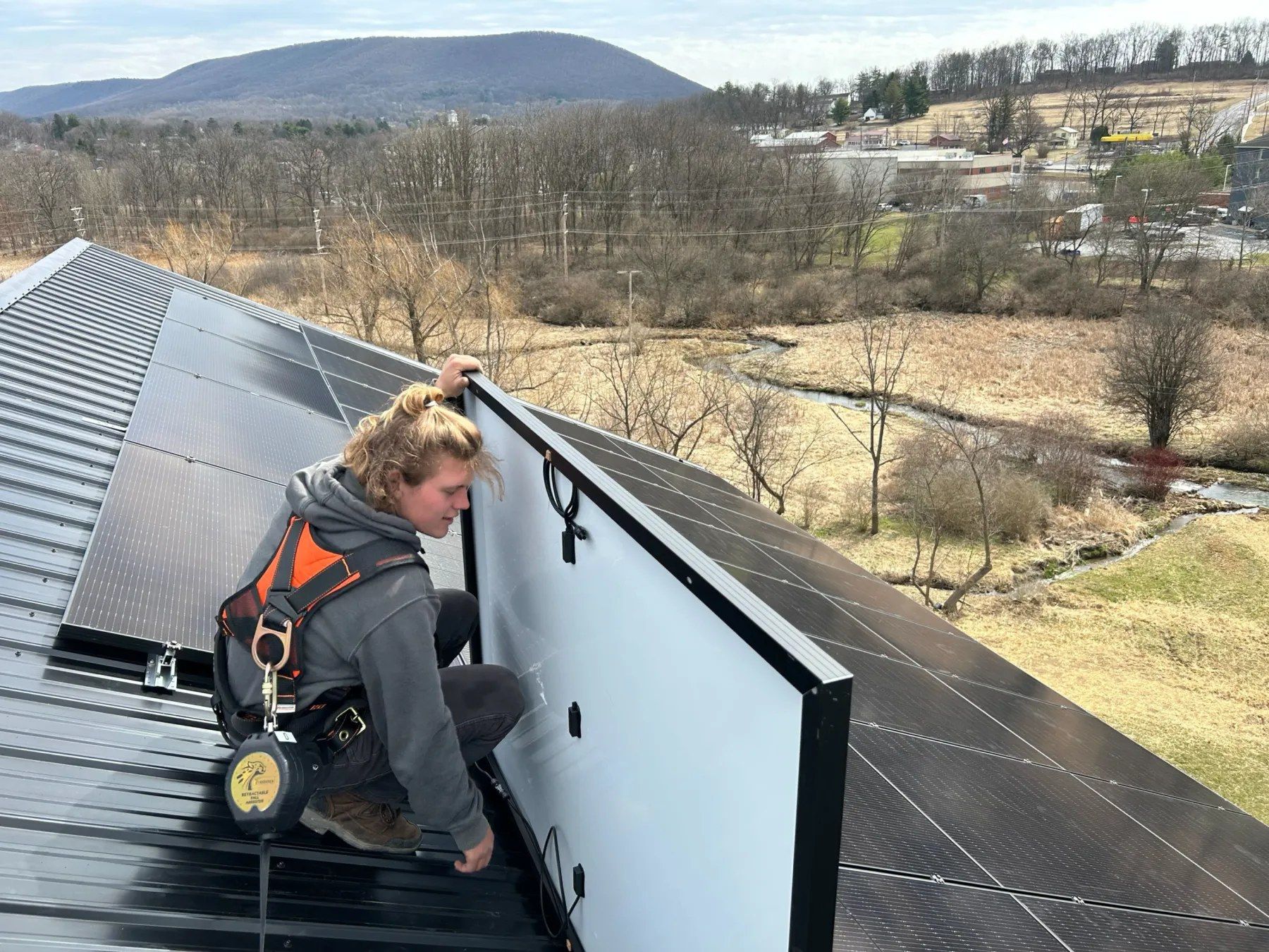 Installer kneeling on a metal roof while setting a solar panel.