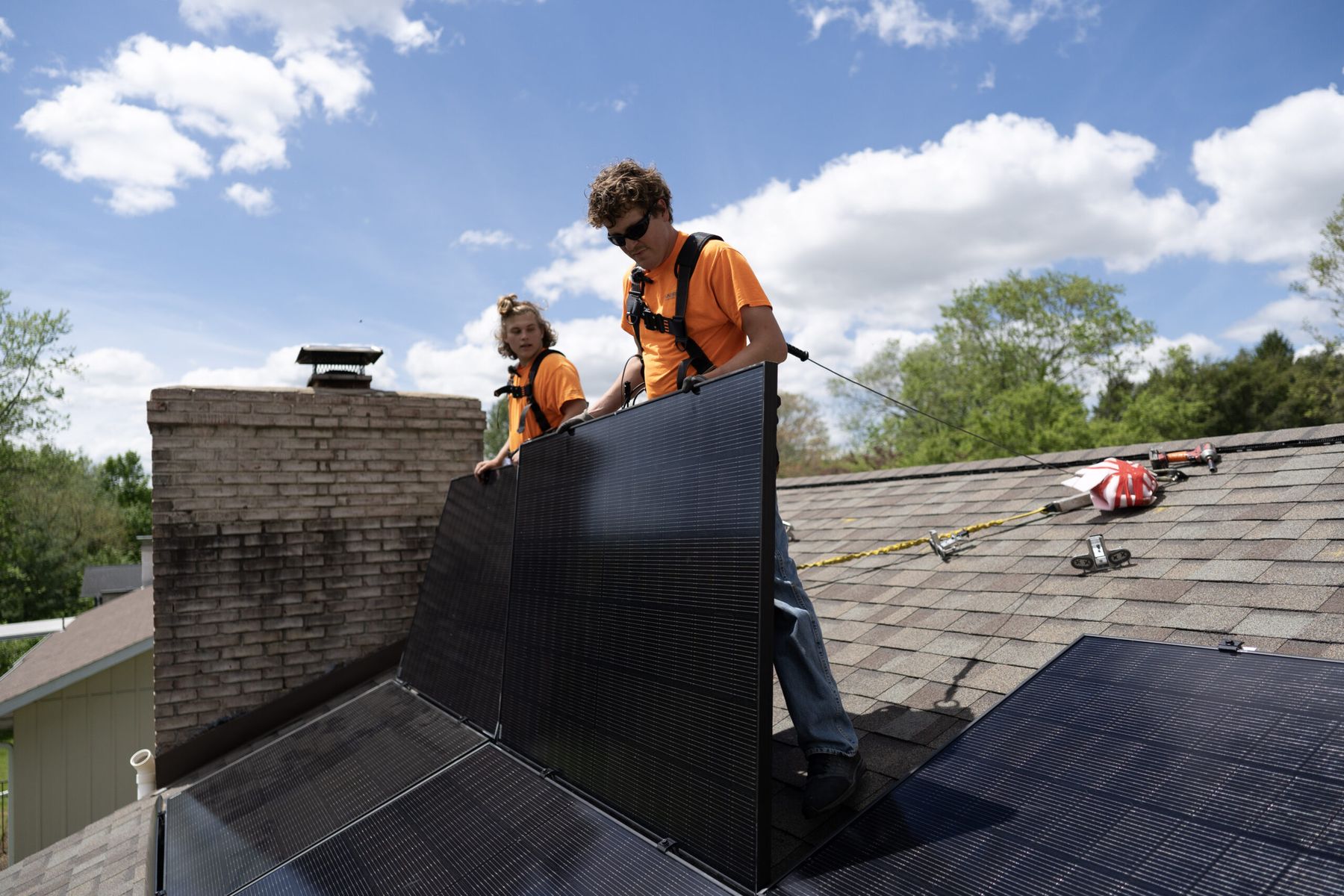 Two installers placing solar modules on a shingle roof.