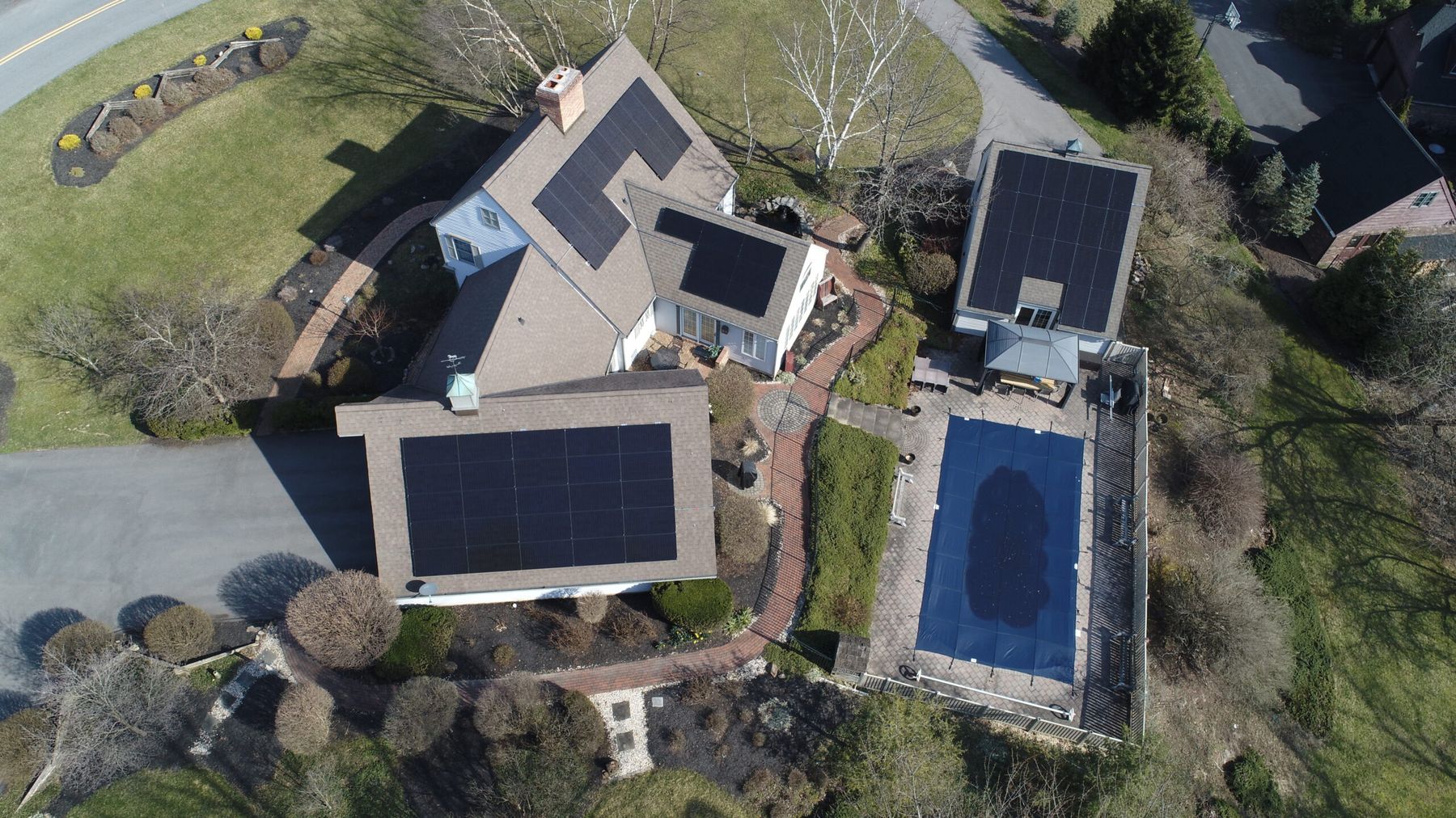 Aerial view of a home with solar arrays on the main roof and pool house.