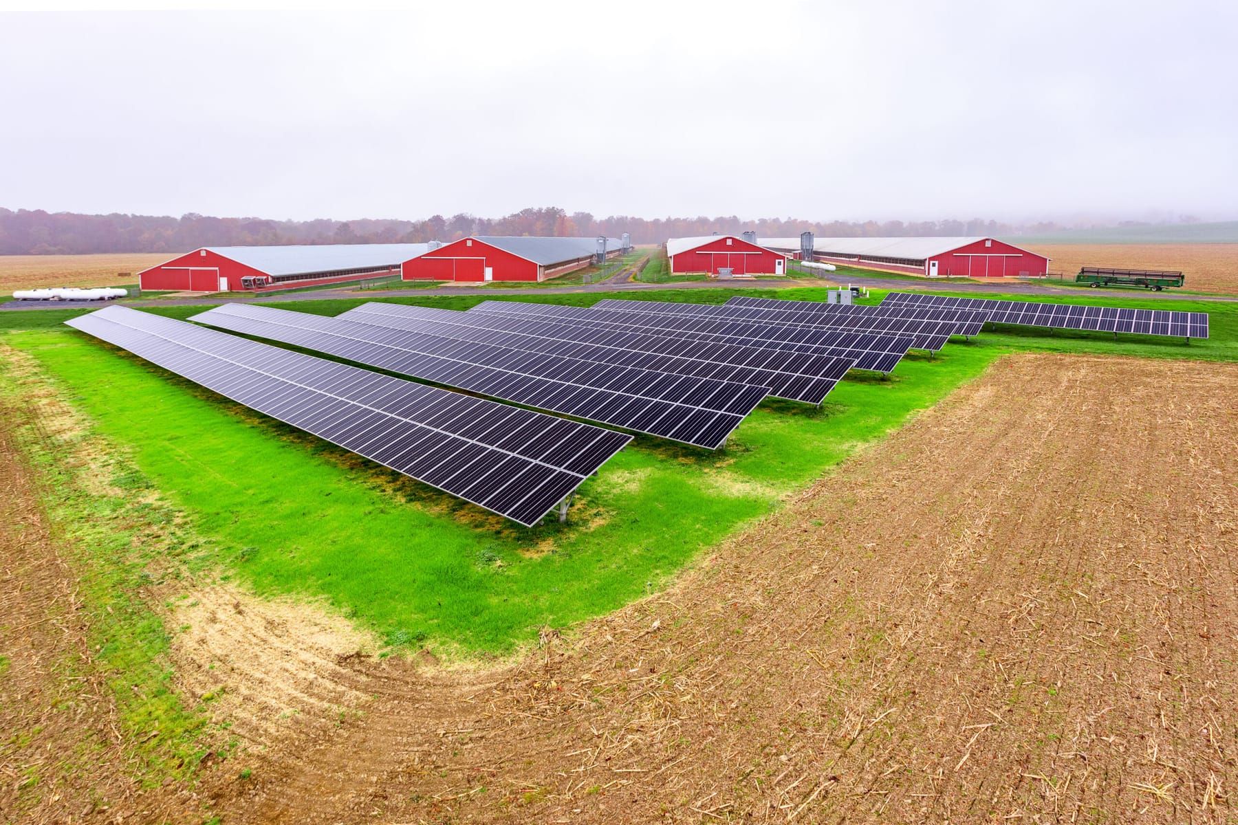 Ground-mount solar array in a field in front of red agricultural barns.